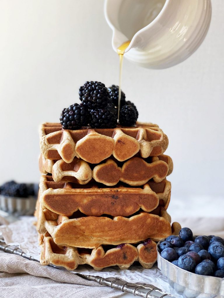stack of high protein paleo waffles with syrup pouring from creamer