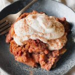 whipped coconut cream on top of apple crumble and sprinkled with cinnamon