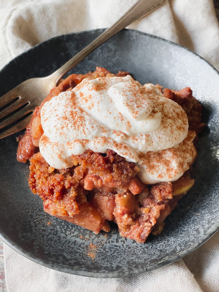 whipped coconut cream on top of apple crumble and sprinkled with cinnamon