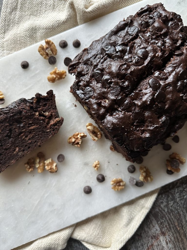 loaf of super dark chocolate banana bread with one slice cut and scattered chocolate chips and walnuts