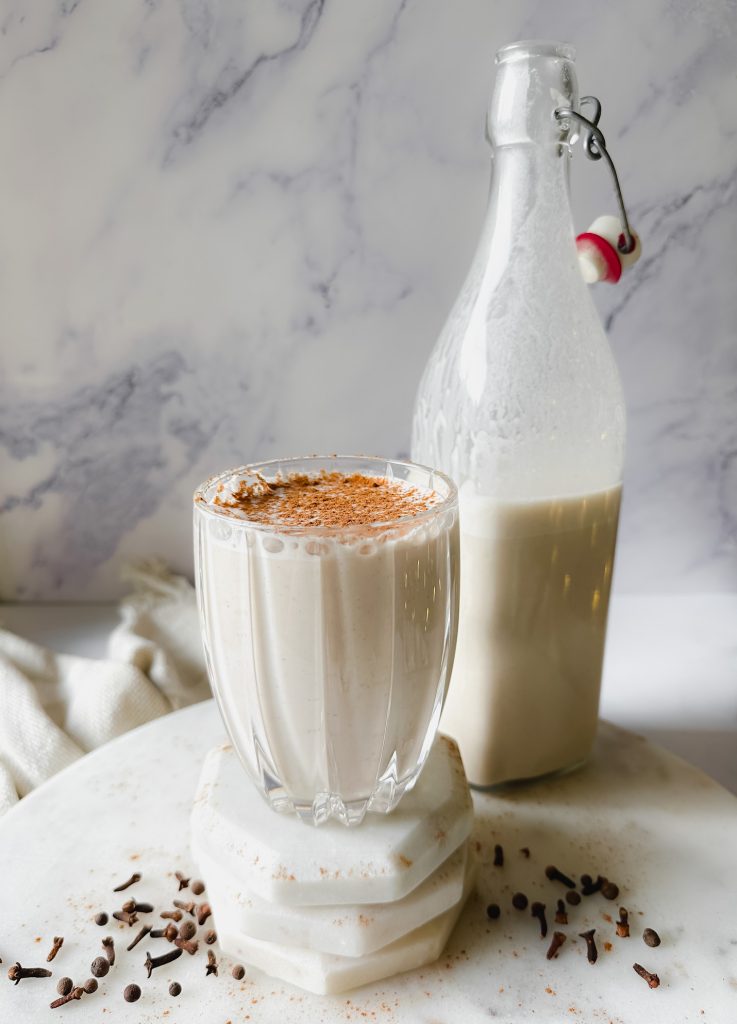 glass of eggnog with bottle of eggnog nearby