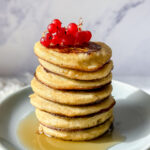 stack of banana pancakes with red currants and maple syrup on top