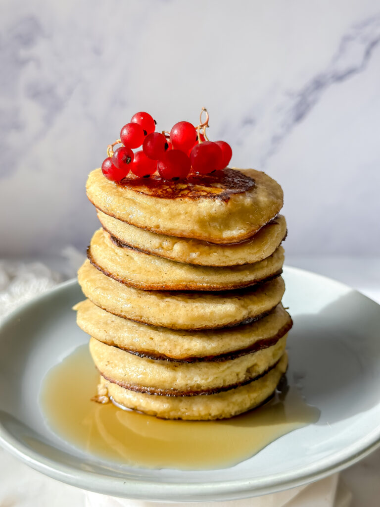stack of high protein banana pancakes with red currants and maple syrup on top