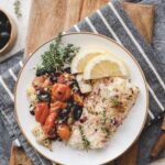 white plate with mediterranean baked white fish and roasted tomatoes, olives, and artichokes
