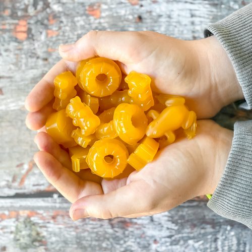 close up of child's hands holding a pile of bright yellow gummies in various shapes