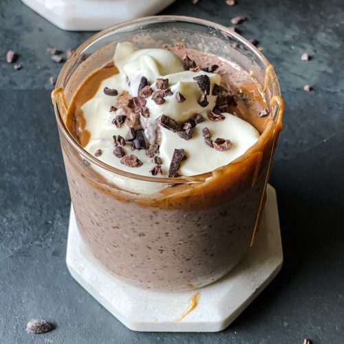 close up of a glass jar containing chocolate pudding textured No Oats with peanut butter, yogurt and cacao nibs on top