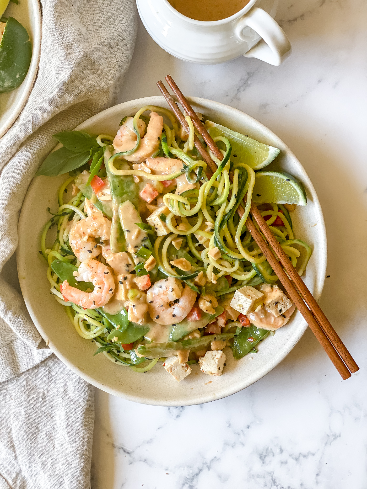 bowl of zucchini noodles covered in peanut sauce, tofu, snow peas, and shrimp