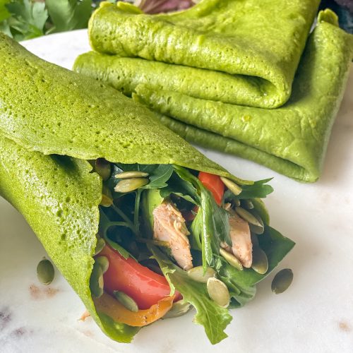 close up view of vibrant green tortilla wrap rolled up with sandwich filling, 2 folded tortillas nearby