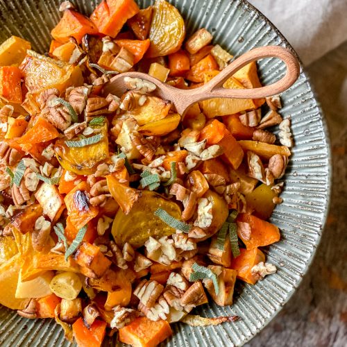 bowl. of diced roasted root vegetables in autumn colors, topped with chopped pecans