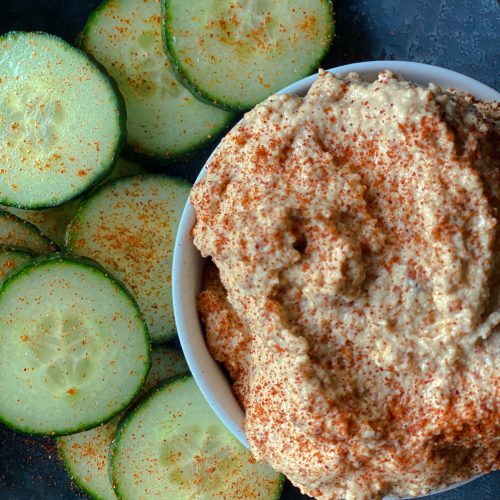 dish of bitchin sauce on a plate with sliced cucumbers and sprinkled with smoked paprika