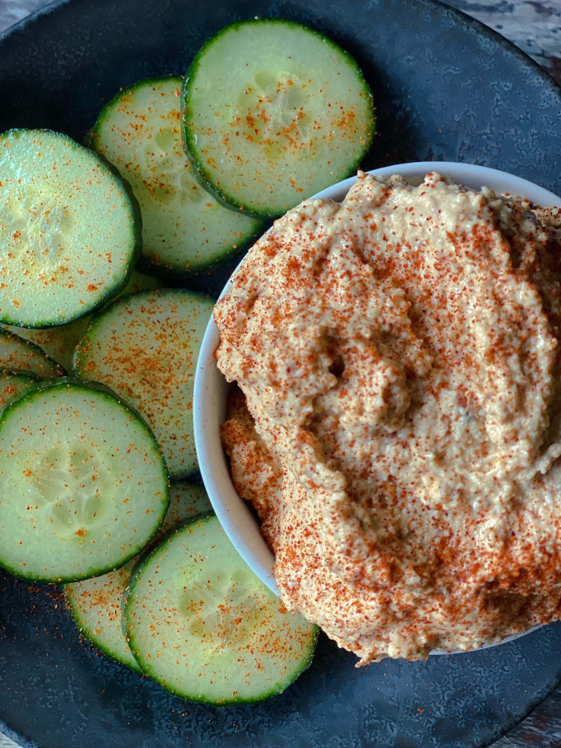 dish of bitchin sauce on a plate with sliced cucumbers and sprinkled with smoked paprika