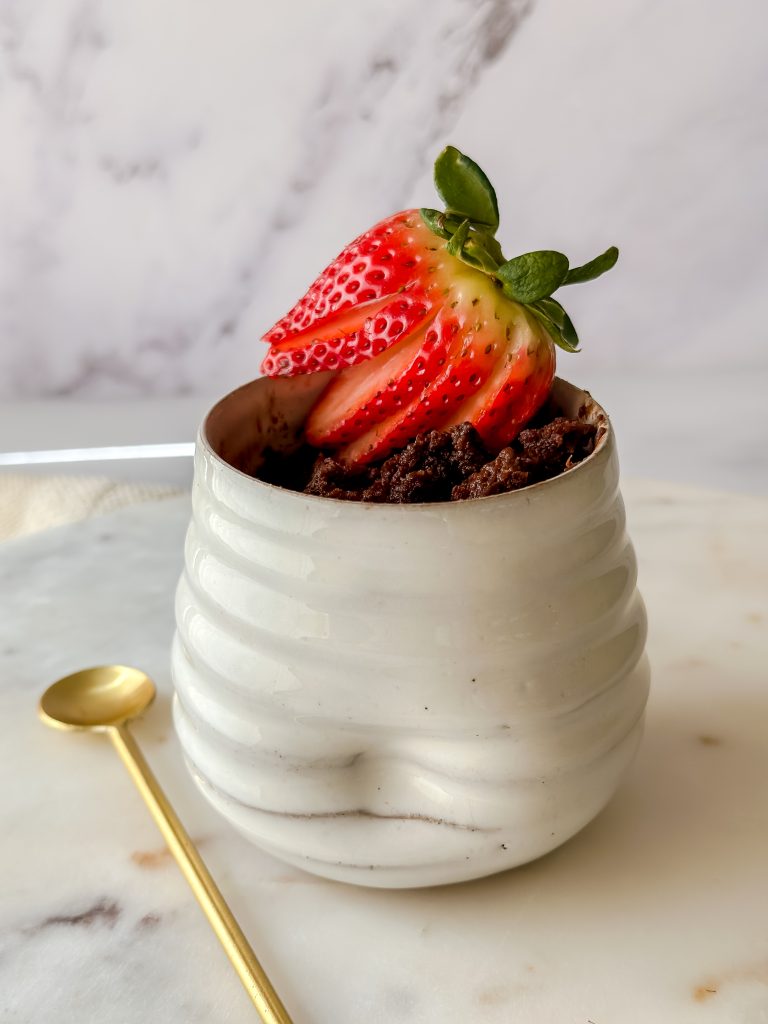 photo of a brownie in a mug topped with sliced strawberries