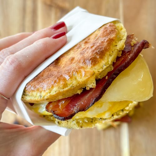 hand holding a breakfast sandwich- homemade english muffin, egg, cheese, bacon