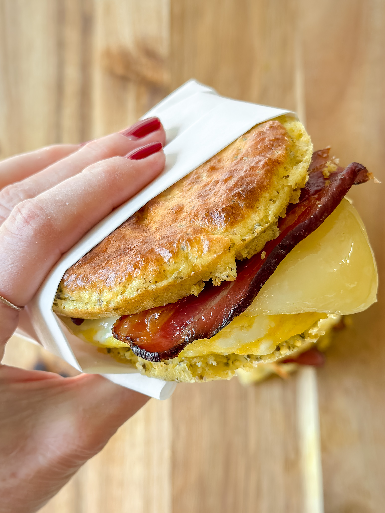 hand holding a breakfast sandwich- homemade english muffin, egg, cheese, bacon