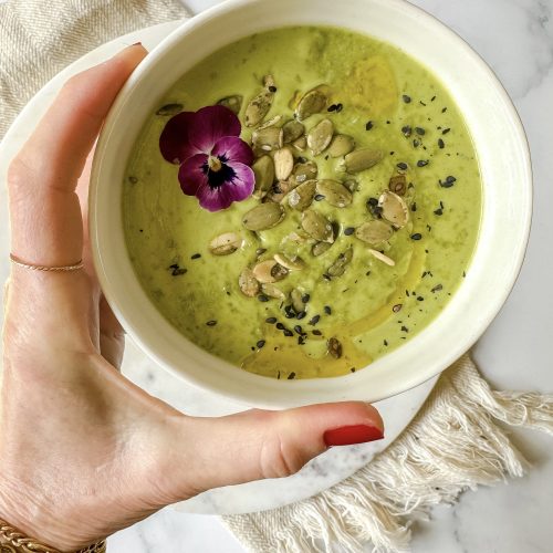 Bowl of green soup topped with pepitas, sesame seeds and edible flower