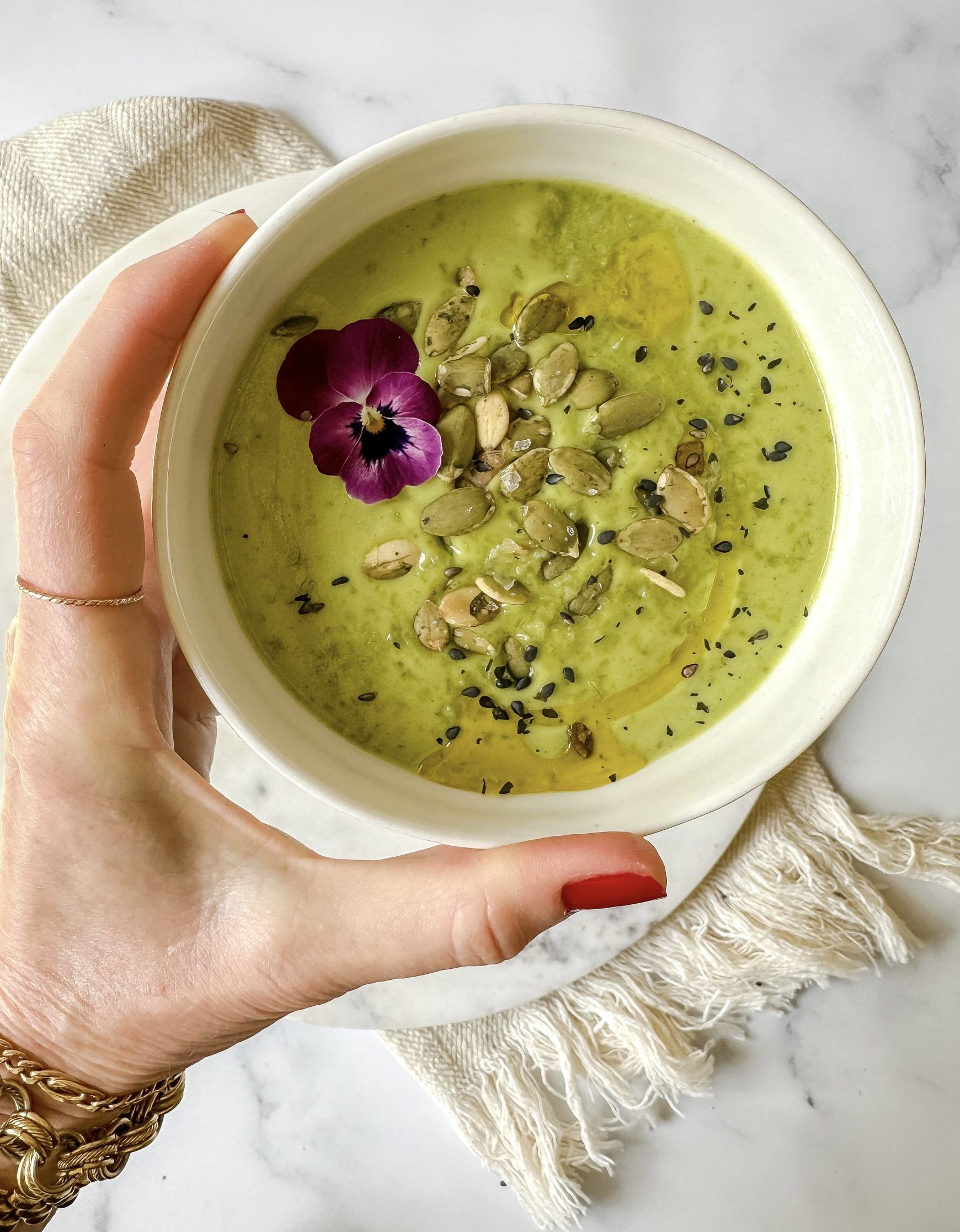 Bowl of green soup topped with pepitas, sesame seeds and edible flower