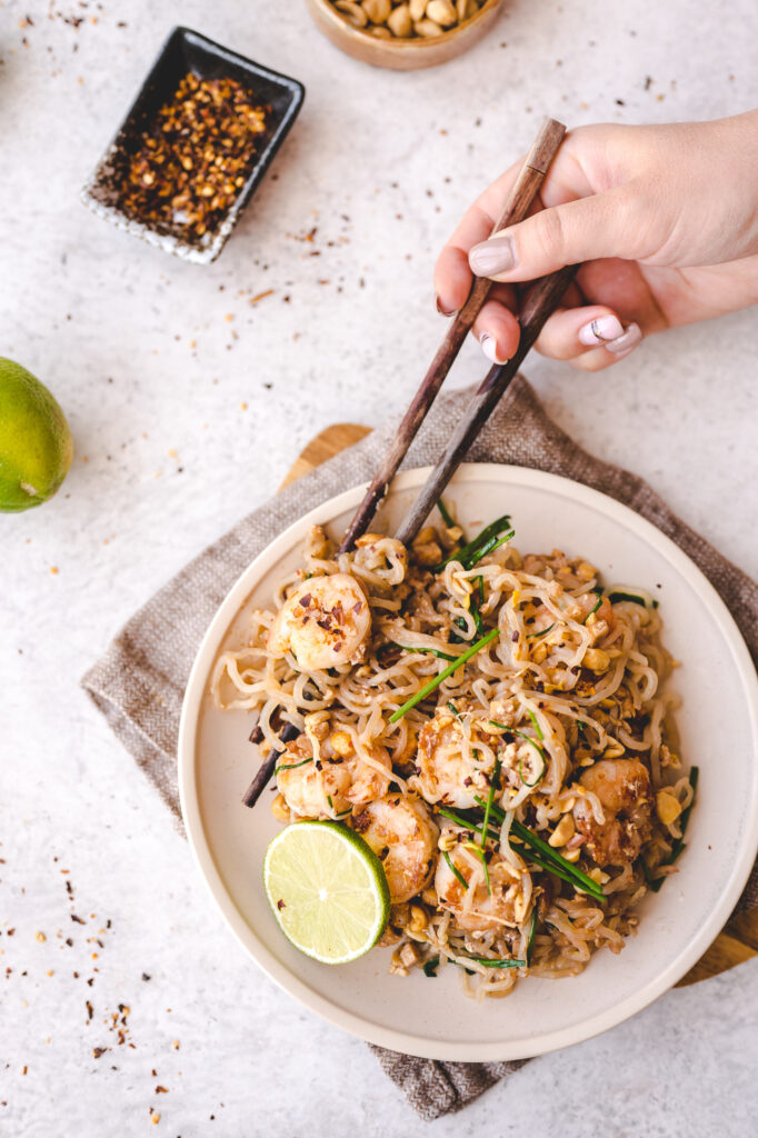 plate of pad thai with lime wedge and hands holding chopsticks